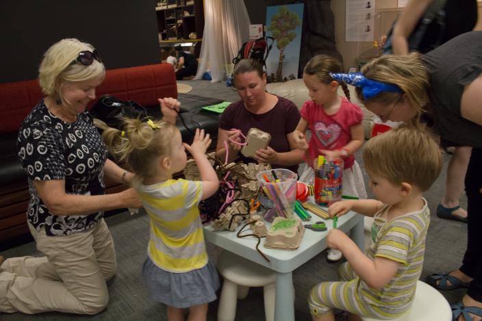 three toddlers and two adults sit around a table crafting